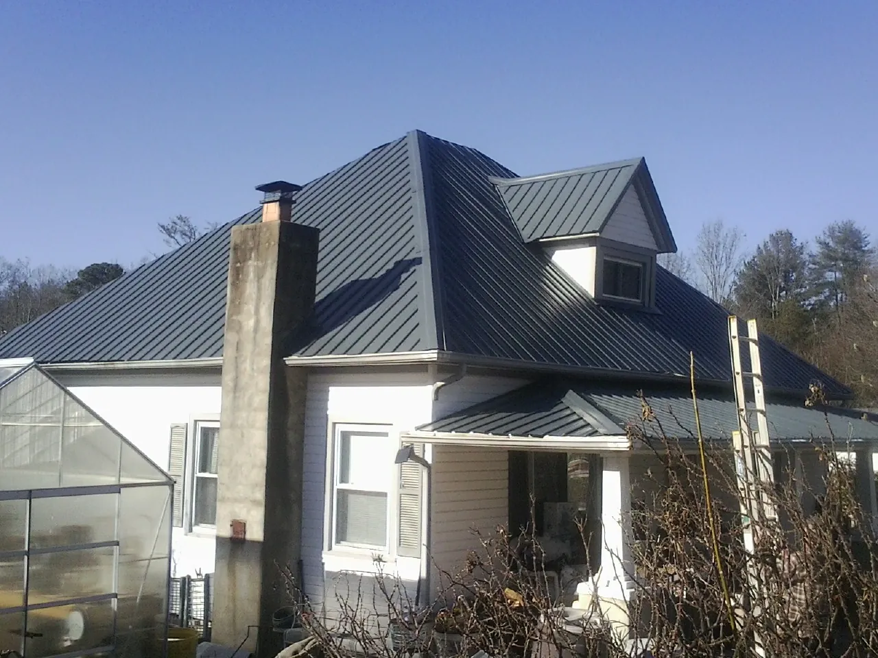 Dark blue standing seam metal roof on a white farmhouse with dormer in Woodland